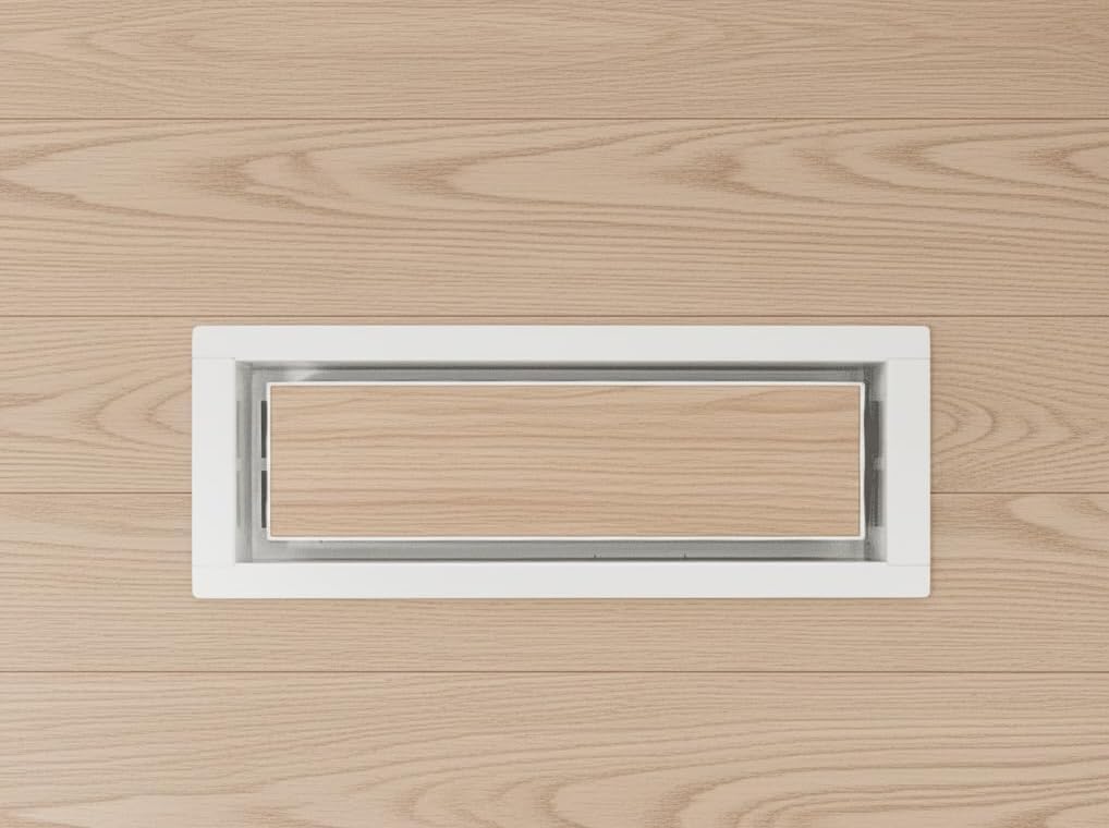 White drop-in metal floor vent installed in light flooring — Khan Supply CO