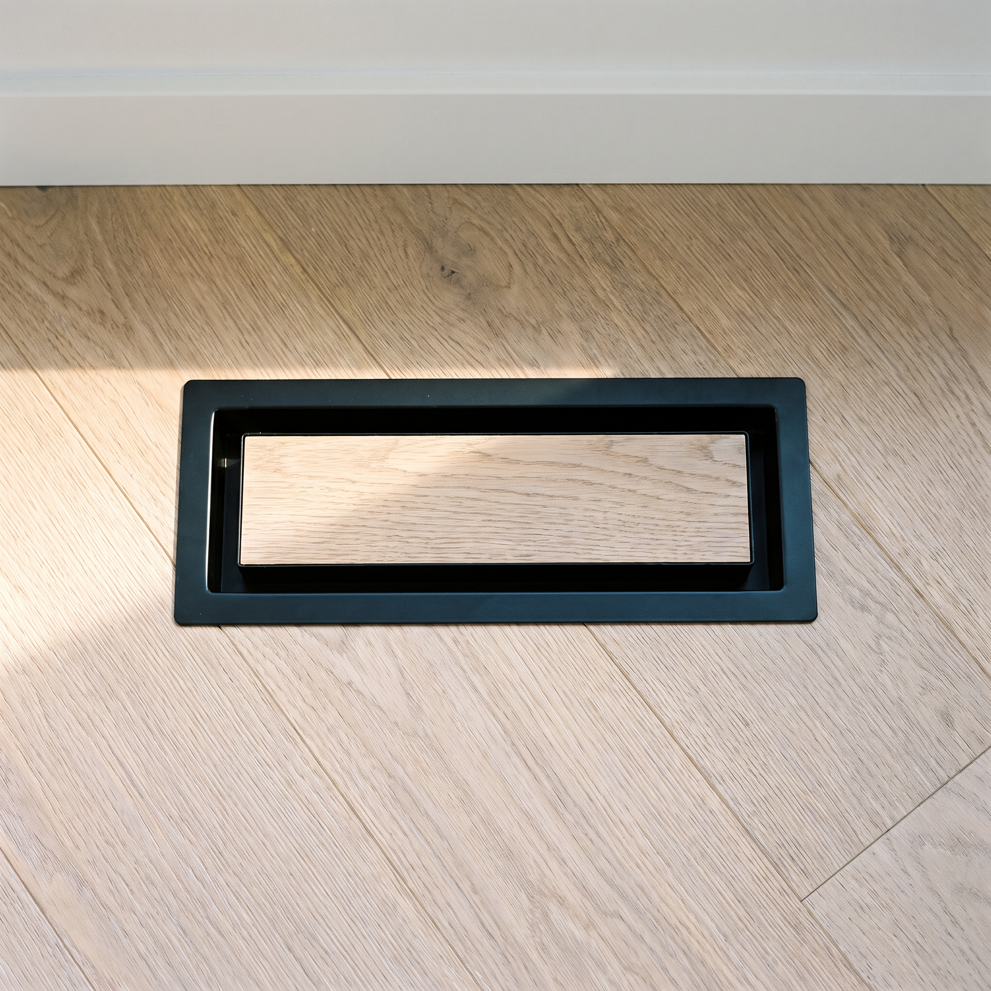 Black metal drop-in floor vent installed flush in light hardwood flooring — Khan Supply CO
